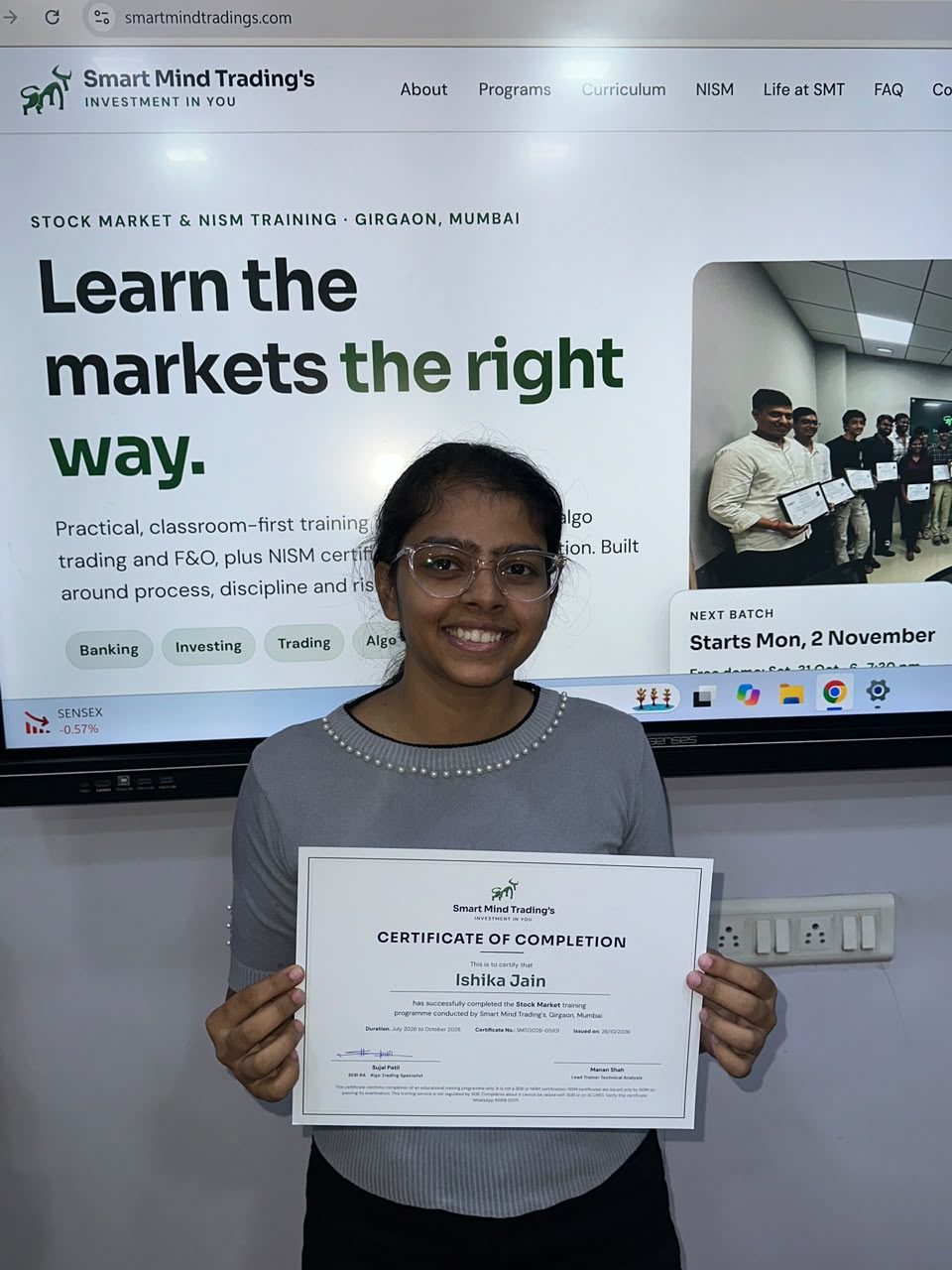 SMT student Ishika holding her Certificate of Completion in the SMT classroom